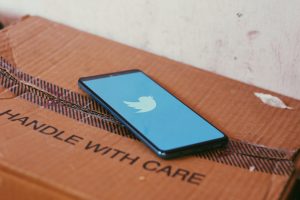 Phone with Twitter logo displayed on it, placed on a cardboard box with a "handle with care" letters on it implying brand trust building