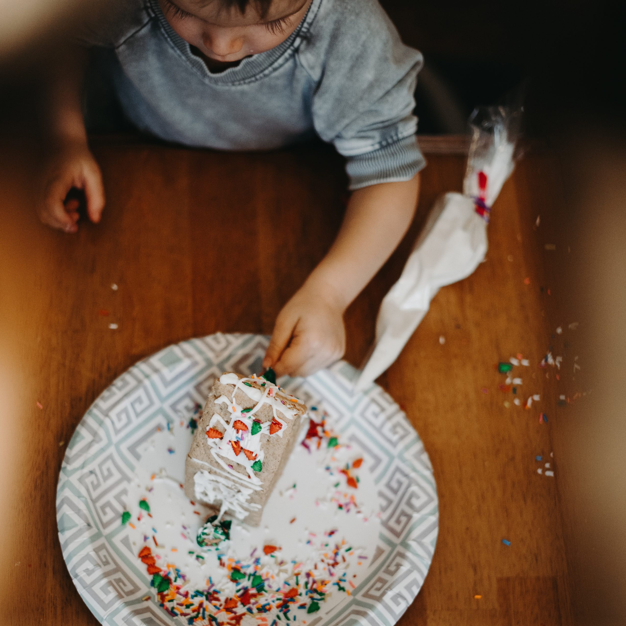little boy decorating a cake with sprinkles and whipped cream